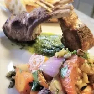 Plated rack of lamb with green sauce and roasted vegetables.