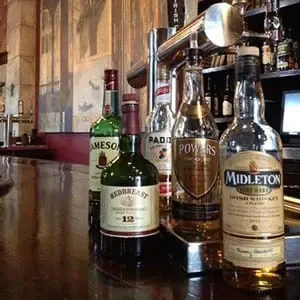 Irish whiskey bottles on a dark wooden bar in a dim pub.