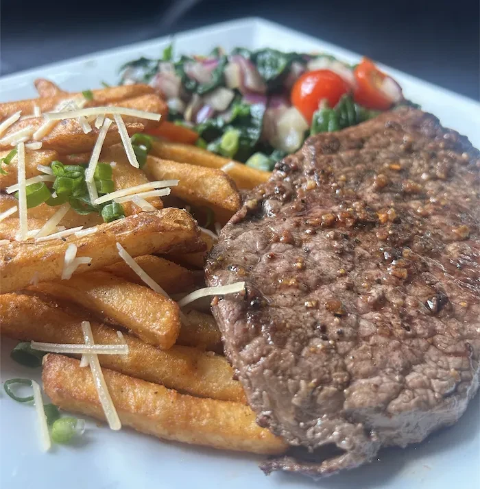 A well-cooked steak, cheesy fries, and a fresh side salad.