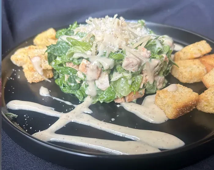 Caesar salad with chicken, Parmesan, croutons, on a black plate.