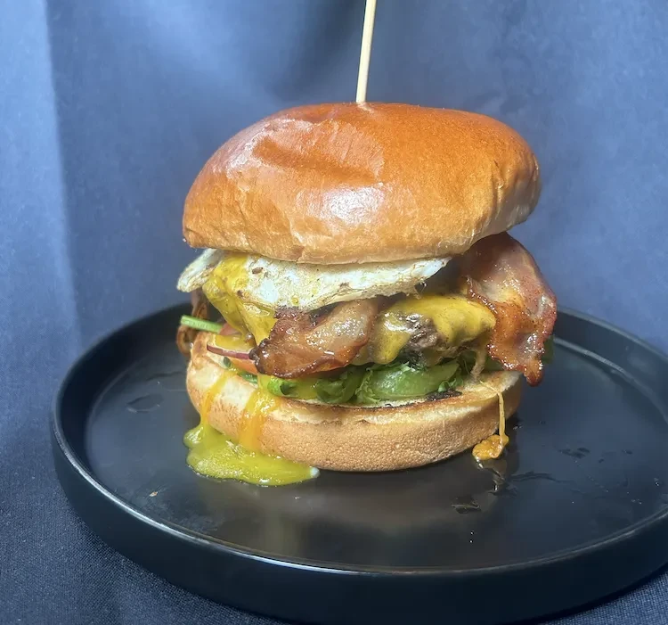 Stacked burger with bacon, fried egg, melted cheese, and dripping yolk.