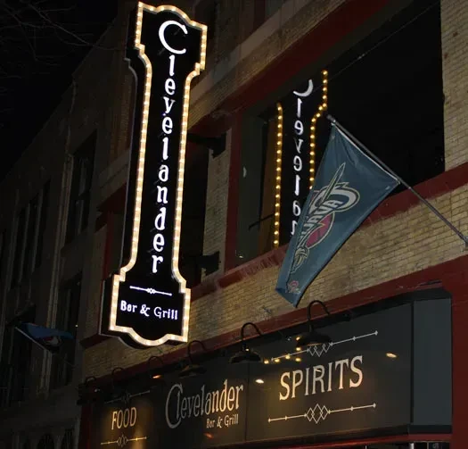 Illuminated Clevelander Bar & Grill signs, brick building, and logo at night.