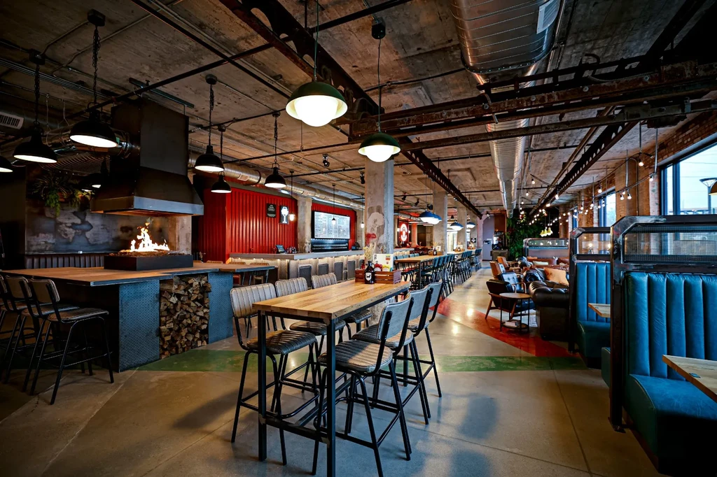Industrial restaurant interior with exposed ceiling, central fireplace, and diverse seating.