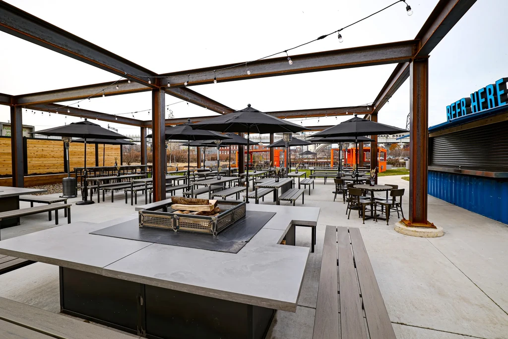 Empty outdoor beer garden with tables, fire pit, and "BEER HERE" bar.