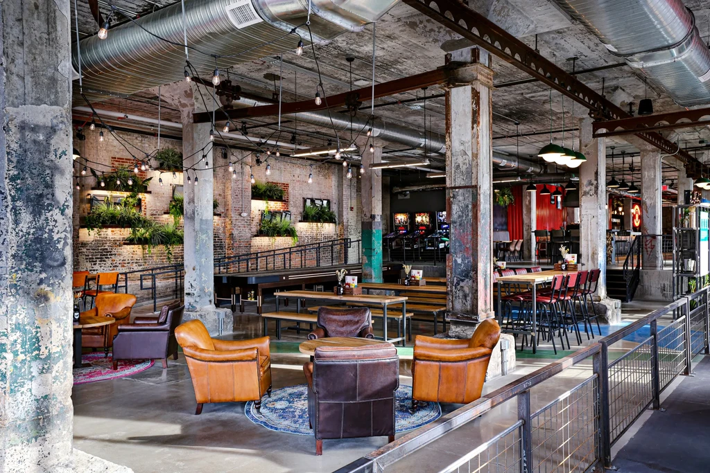 Multi-level industrial restaurant interior with exposed brick, string lights, arcade games.