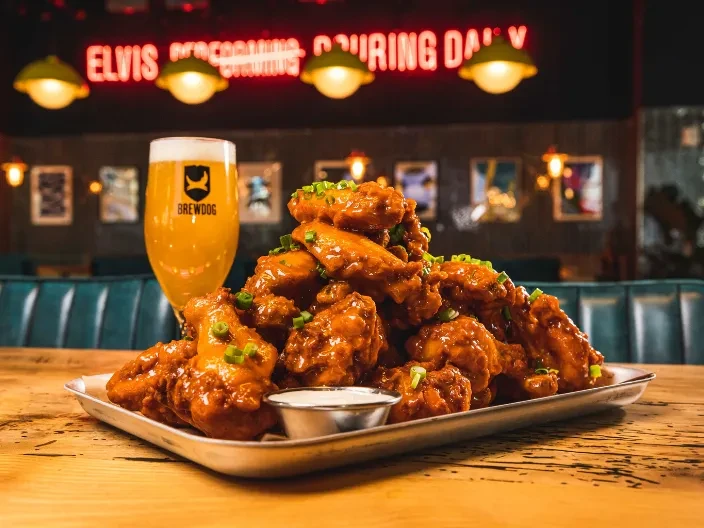 Saucy buffalo wings with green onions, dipping sauce, and BrewDog beer.