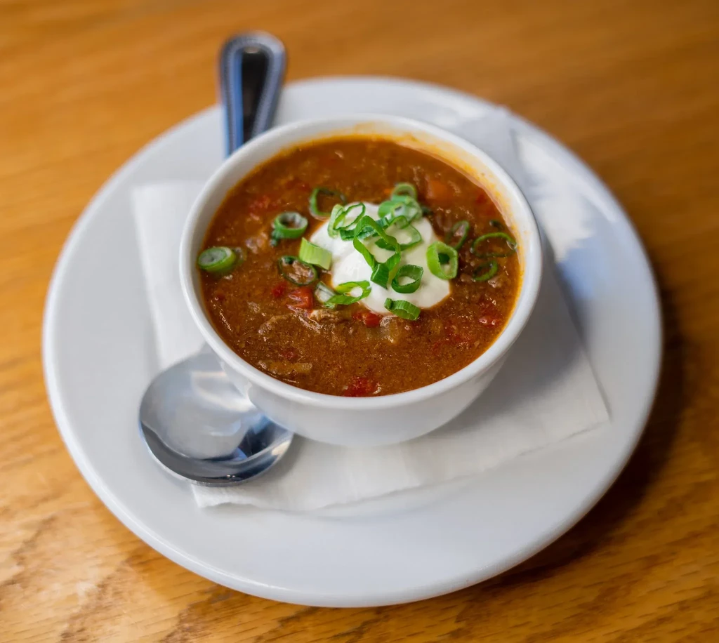 Hearty chili in a white bowl, topped with sour cream and green onions.