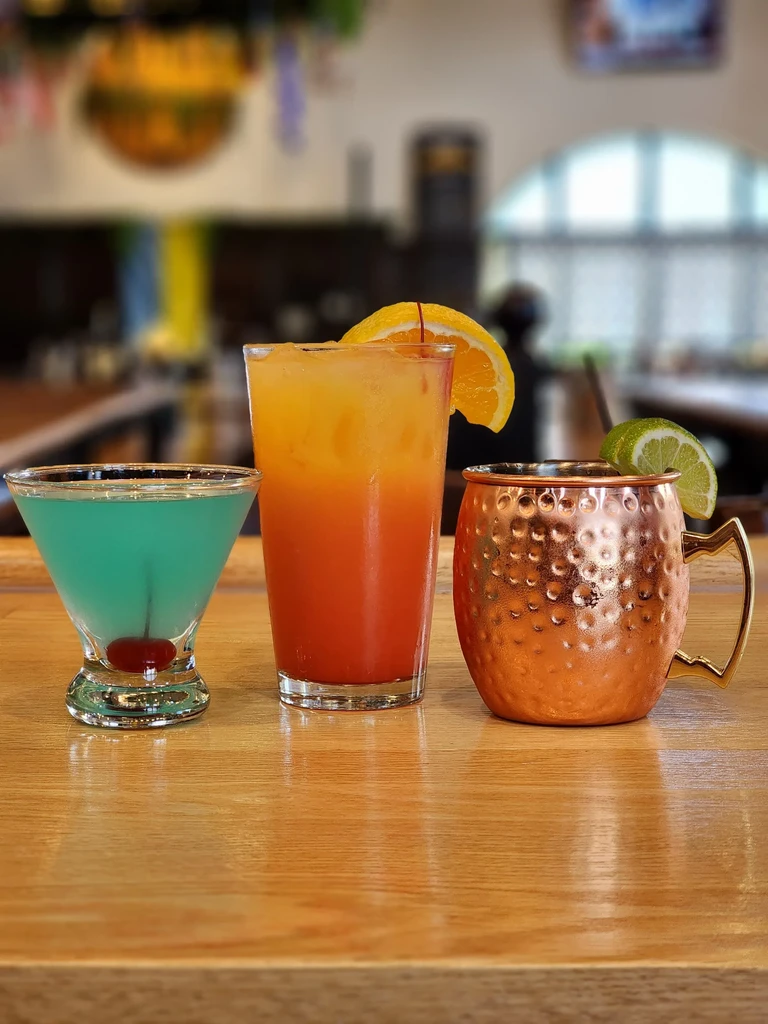 Three distinct cocktails: a martini, a layered drink, and a copper mug.