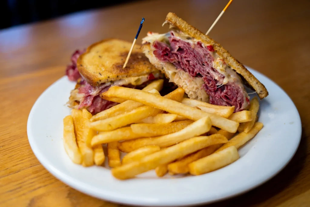 Sliced Reuben sandwich revealing corned beef, sauerkraut, cheese, and fries.
