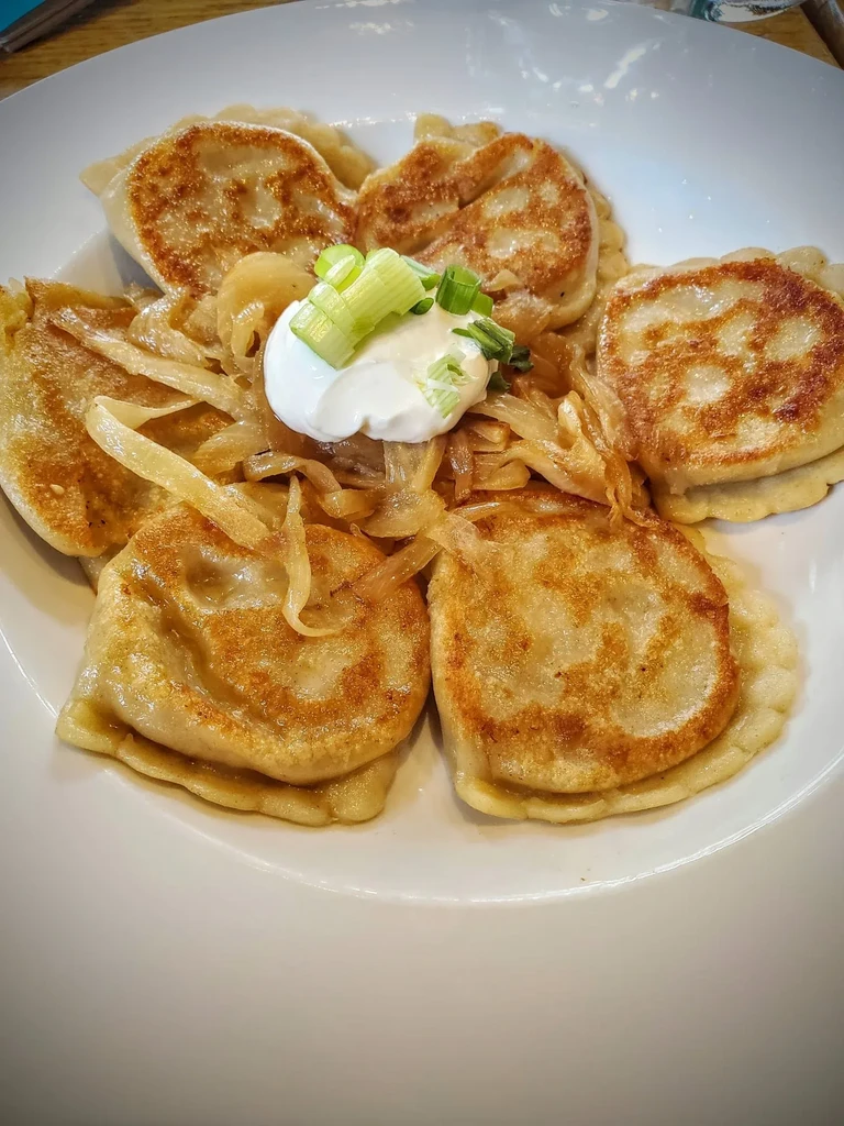 Pan-fried pierogi topped with caramelized onions, sour cream, and chives.