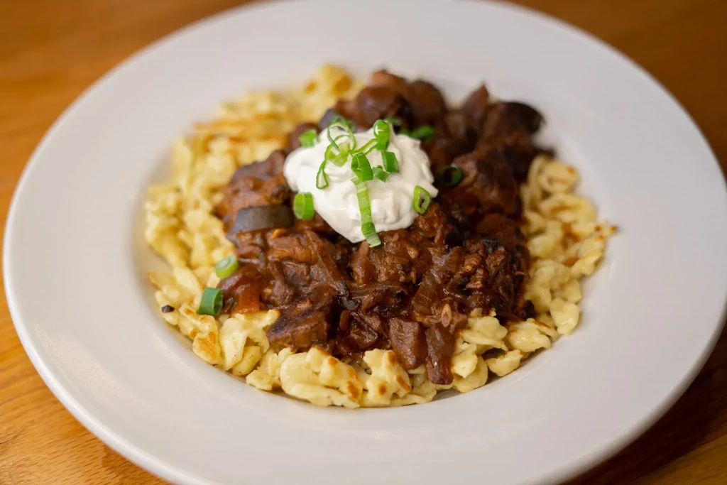 Close-up of goulash with spaetzle, sour cream, and chives.