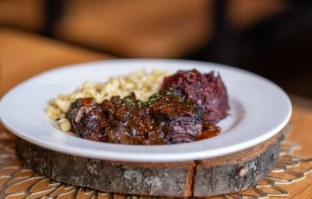 Close-up of braised meat, spaetzle, and cabbage on a white plate.