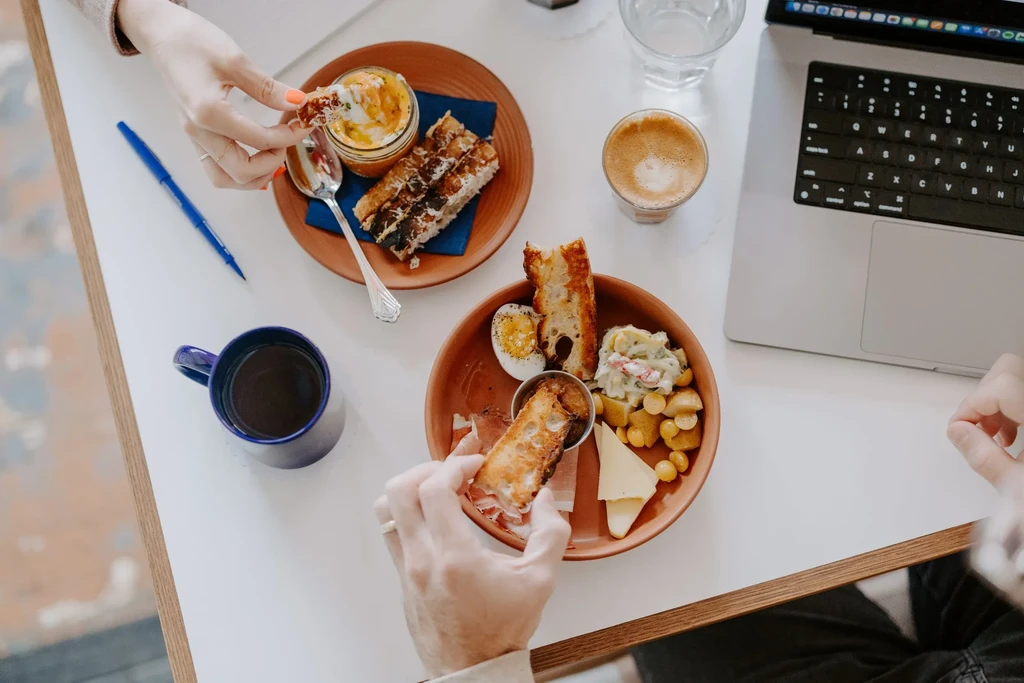 Overhead brunch table with hands, food, drinks, and a laptop.