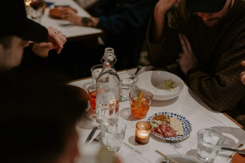 Intimate evening dining table with cocktails, food, candle, and blurred people.