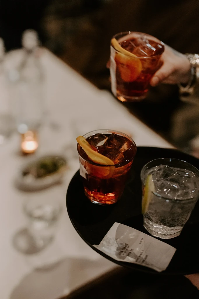 Dimly lit close-up of three drinks on a tray, one served by hand.