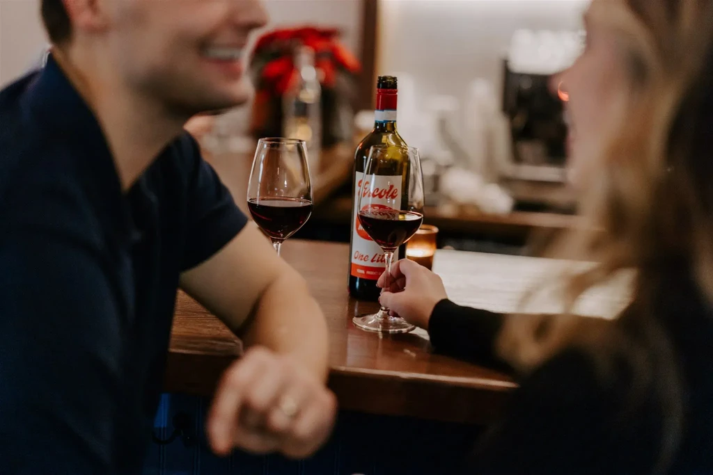 Blurred couple with red wine bottle and two glasses at counter.