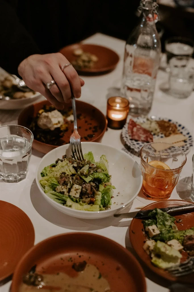 Dining table from above with a hand eating salad, charcuterie, and cocktails.