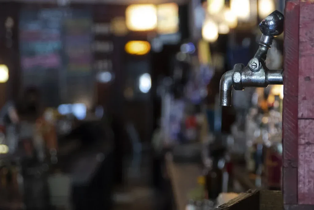 Vintage metal tap on wood, with blurred bar background.