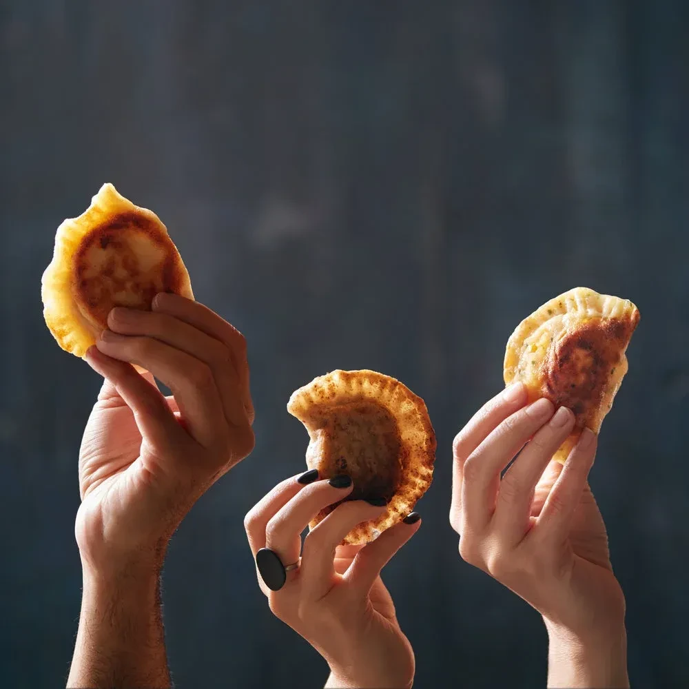 Three hands hold golden-brown fried pastries against a dark background.