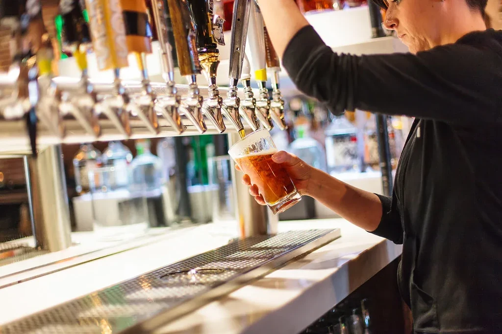Bartender in profile pours foamy amber beer from a tap.