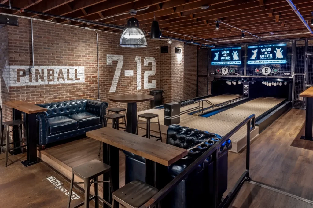 Industrial entertainment venue with mini-bowling, brick walls, and event screens.