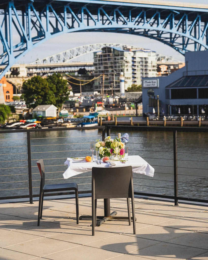 Outdoor dining table for two, overlooking a city skyline and arch bridge.