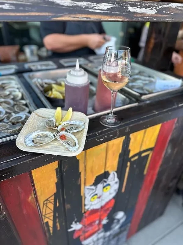 Three oysters, wine, and painted bar at a bustling oyster stand.