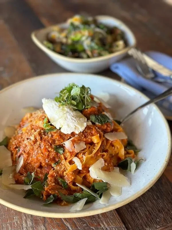 Close-up of pasta with Bolognese sauce, parmesan, basil, and microgreens.