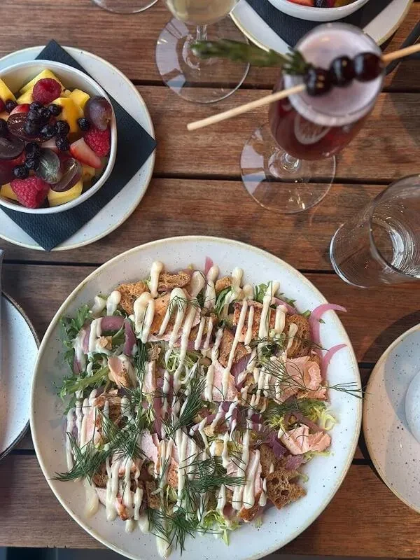 Top-down: Wooden table with salmon salad, fruit salad, drinks.