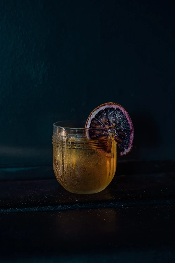 Cold golden amber cocktail with dried citrus garnish on a dark background.