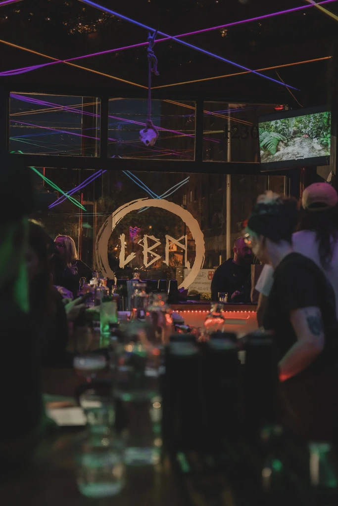 Dimly lit bar with patrons, neon lights, and an 'LBN' window logo.