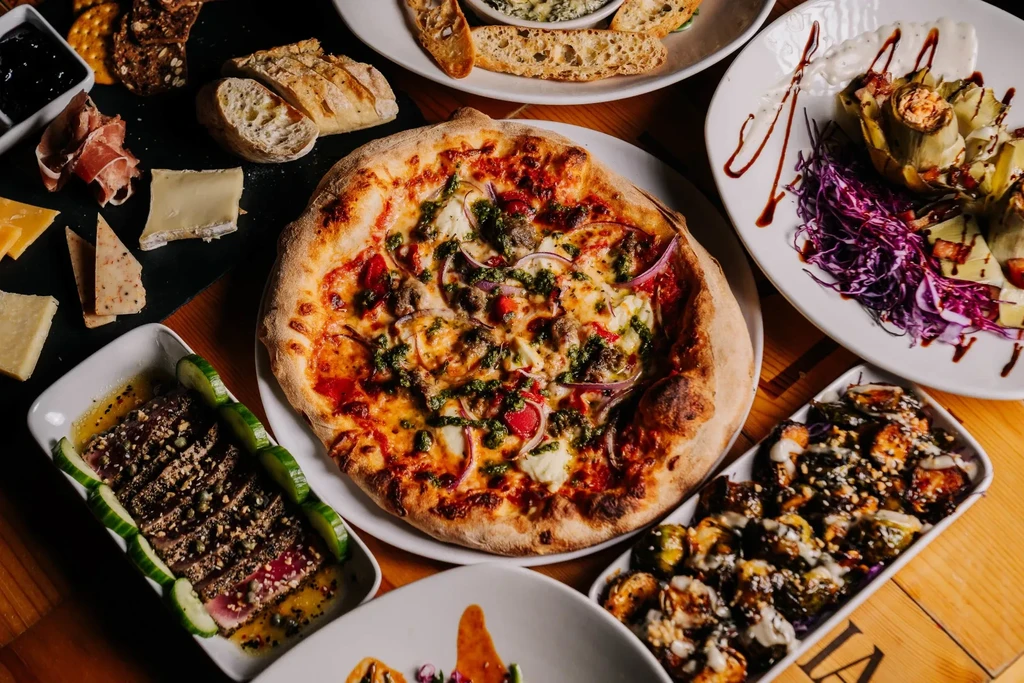Overhead shot of pizza, charcuterie board, seared tuna, and roasted vegetables.