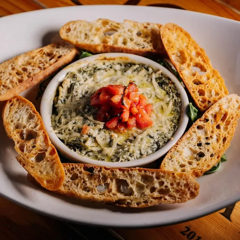 Overhead creamy green dip with tomatoes and toasted baguette slices.