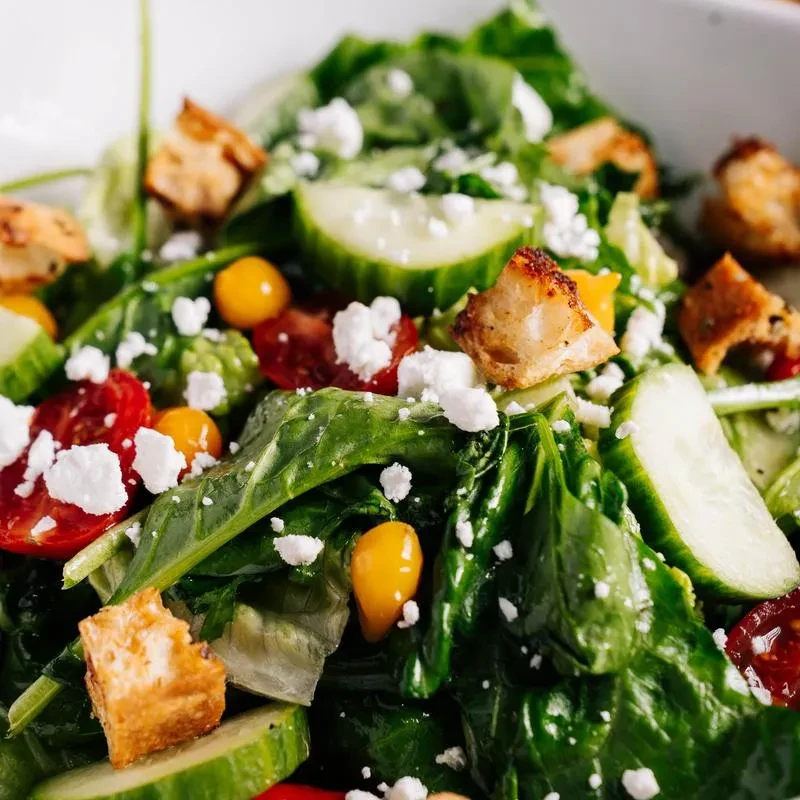 Fresh, colorful salad with greens, tomatoes, feta, and croutons in a bowl.