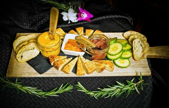 Appetizer board with bread, cucumber, three dips, rosemary, and orchids.