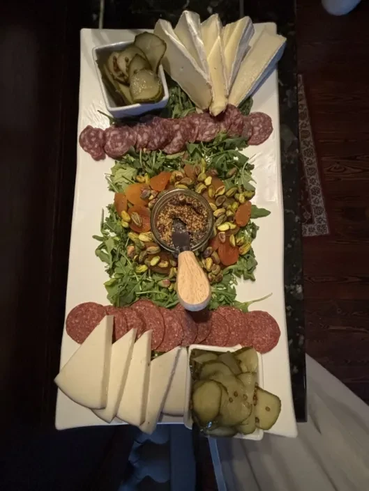 Generously arranged charcuterie board with cheeses, meats, apricots, mustard, pickles.