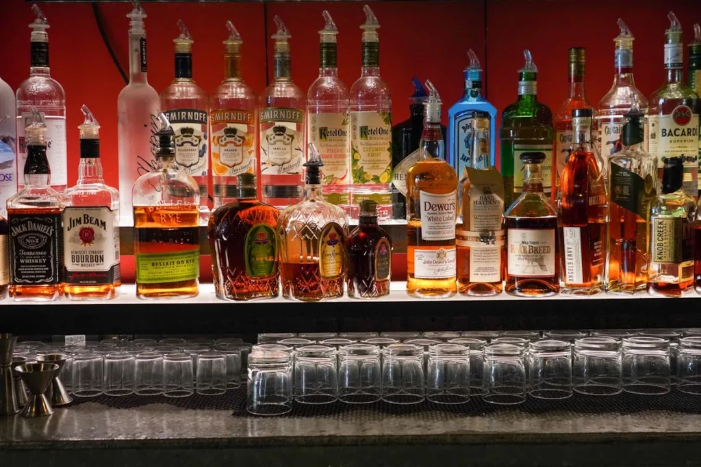 Well-stocked bar with tiered spirit bottles, clean glasses, and red background.