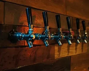 Six polished beer taps mounted on a rustic wooden wall.