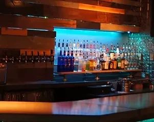 Well-stocked bar counter with teal LED-lit liquor bottles and beer taps.