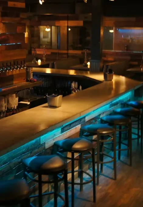 Curved wooden bar counter with blue LED lighting and beer taps.