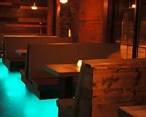 Empty restaurant booths, dark wood walls, blue under-lighting, and table lamp.
