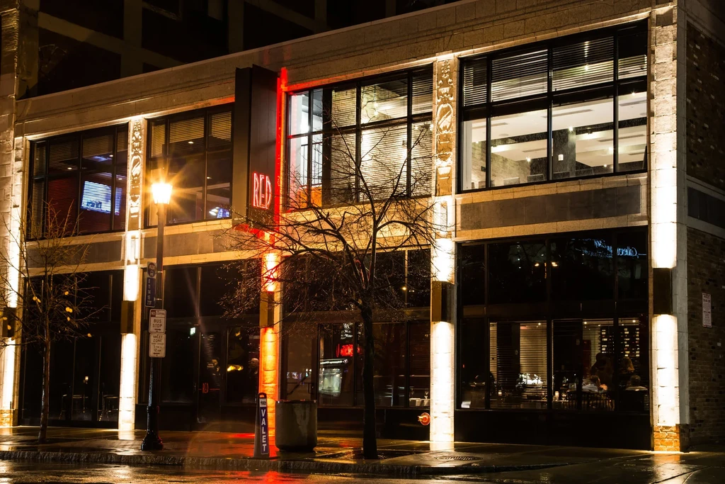 Modern "RED" restaurant building at night with patrons and wet street.