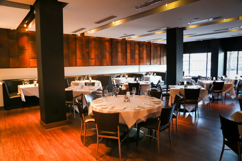 Empty, elegant restaurant with set tables, dark seating, and glowing orange wall.