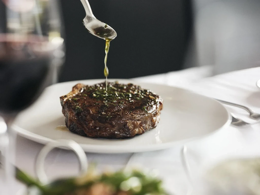 Perfectly cooked steak on plate, spoon actively drizzling herb sauce.