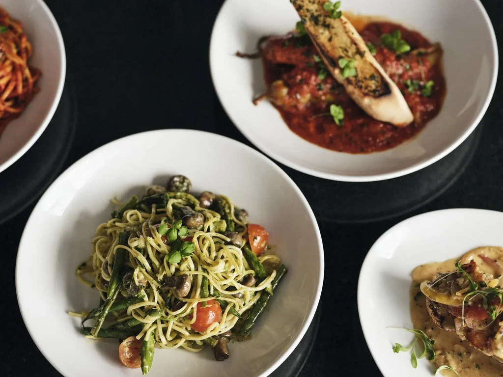 Overhead: Four artfully plated pasta, stew, and protein dishes.