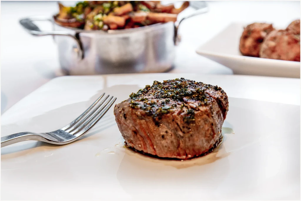Close-up of herb-crusted steak on white plate with fork.