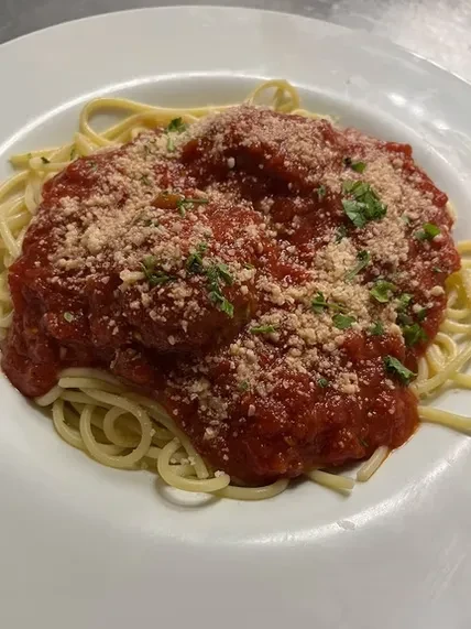 Plate of spaghetti and meatballs with red sauce, cheese, and herbs.