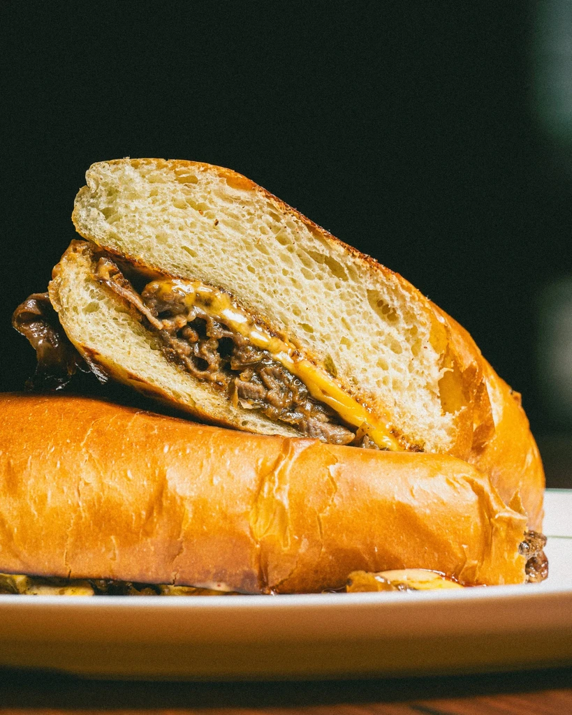 Halved cheesesteak with meat, cheese, and onions on a plate.