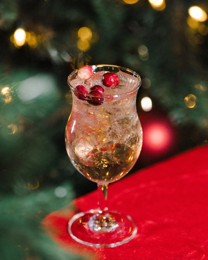 Festive amber cocktail with cranberries and crushed ice, blurred Christmas background.
