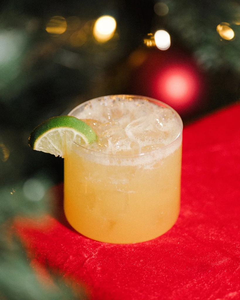 Cloudy yellowish-orange cocktail with lime on a red surface, festive background.